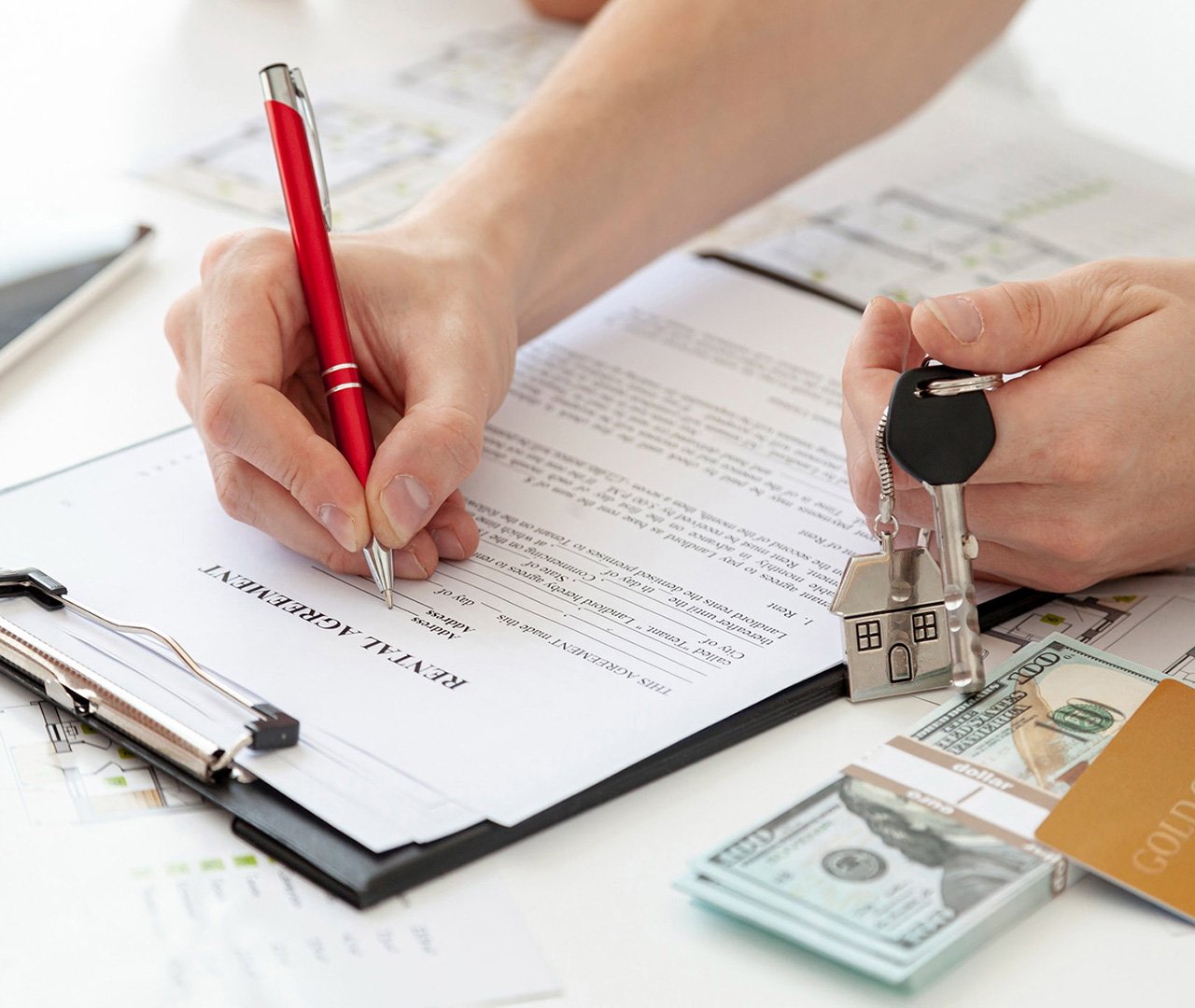Close-up of a client or tenant signing a rental agreement while holding house keys and placing a security deposit or first month's rent.