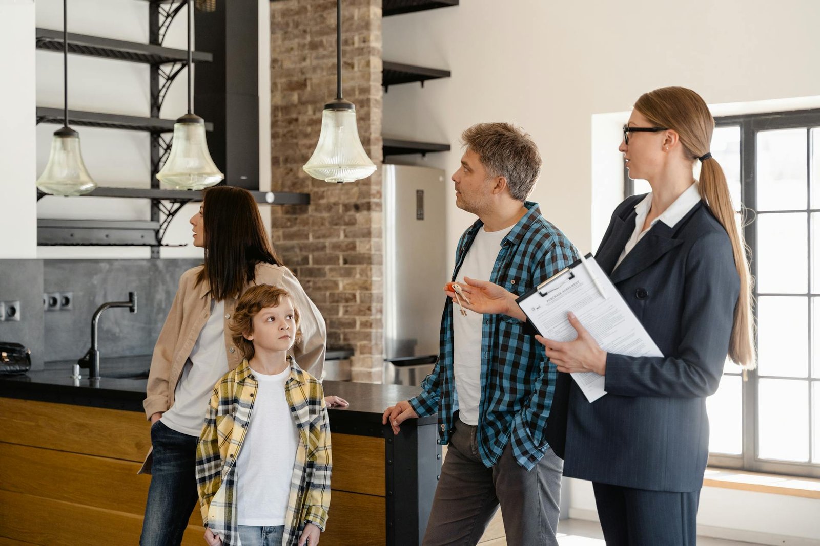 Real estate agent showing a modern, open-concept kitchen and living area to a young family.
